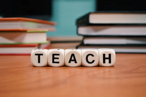 Brainfood Academy Teacher and Tutor Information & Application Link - Teach spelled out in small white blocks on a table in front of two small stacks of books.